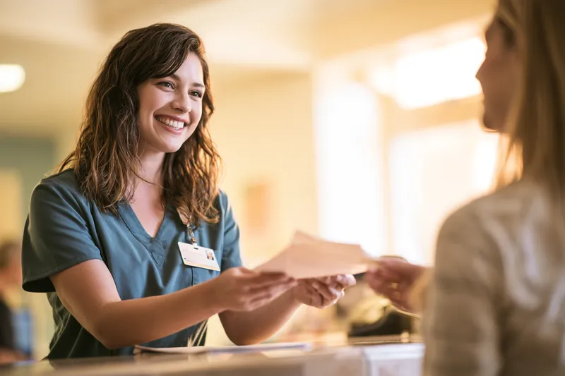 American nurse handing intake paperwork to a patient at a clinic reception